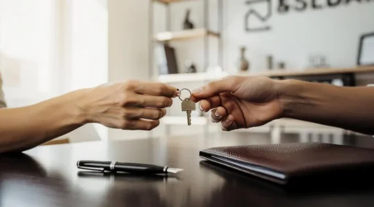 Deux mains échangeant un trousseau de clés au-dessus d'un bureau de notaire, symbolisant la signature de l'acte authentique
